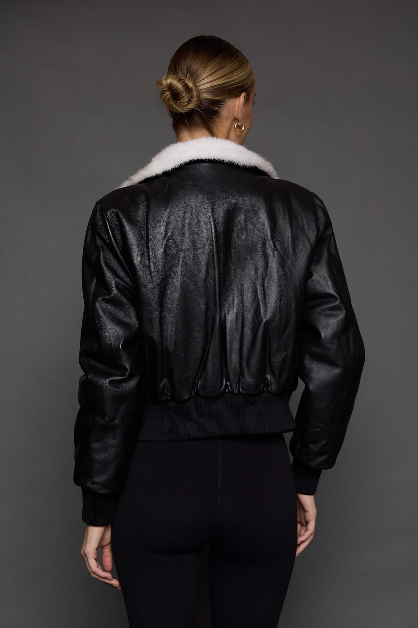 ATHANASIA CROSS MINK JACKET REV BACK the back of a woman in a black leather jacket against a grey background