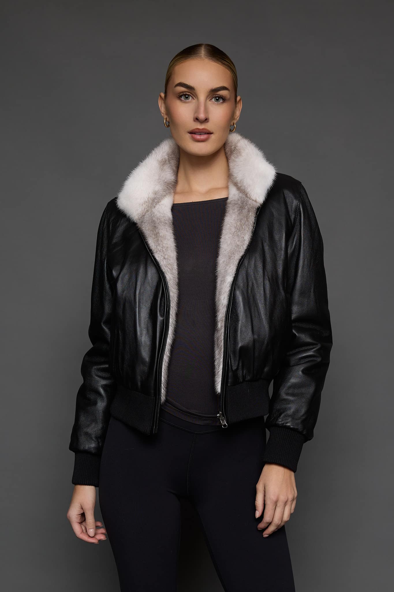 ATHANASIA CROSS MINK JACKET REV FRONT 2 woman in a black leather jacket against a grey background