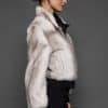 ATHANASIA CROSS MINK JACKET SIDE Profile view of a woman in a white jacket against a grey background