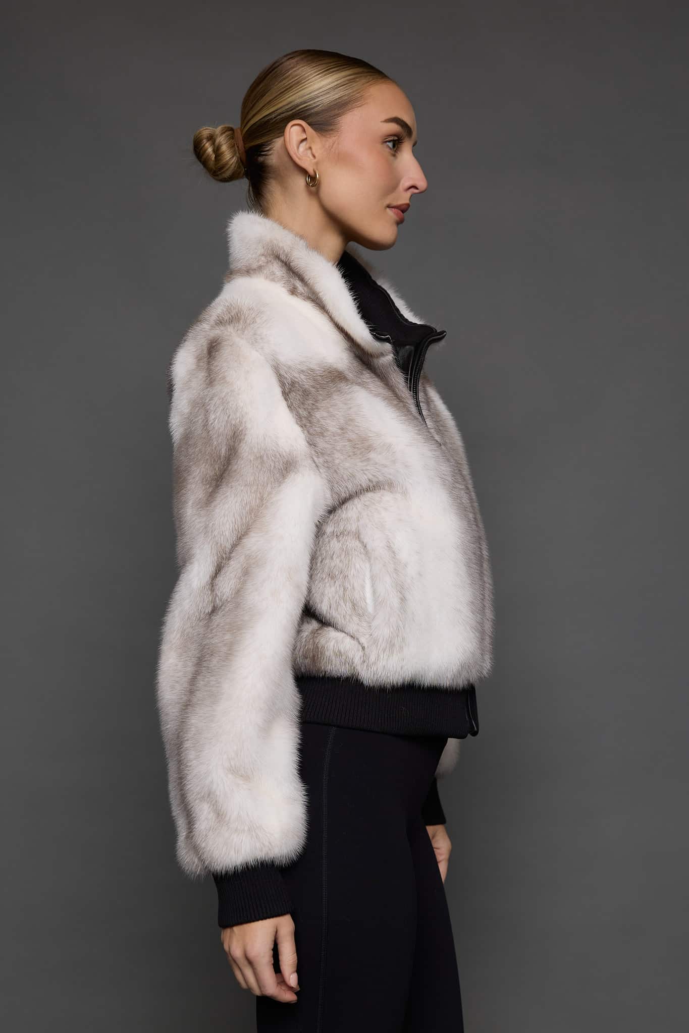 ATHANASIA CROSS MINK JACKET SIDE Profile view of a woman in a white jacket against a grey background