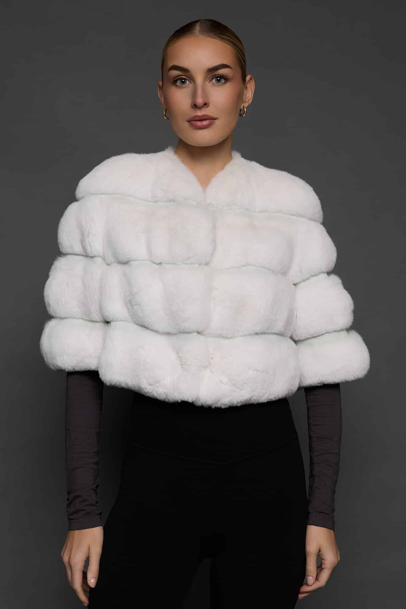 Frontal view of a woman in a white bolero jacket standing against a dark grey background
