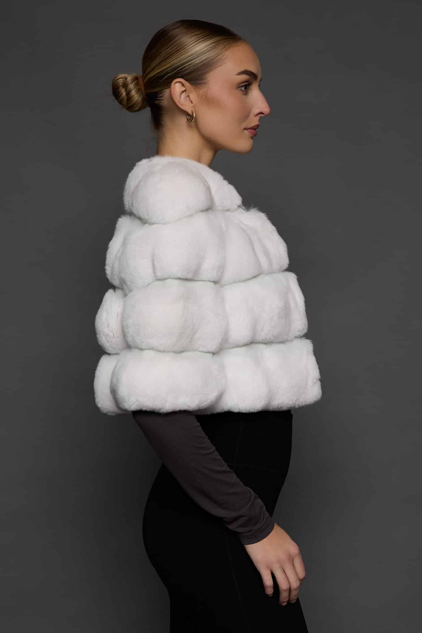 Profile view of a woman in a white bolero jacket standing against a dark grey background