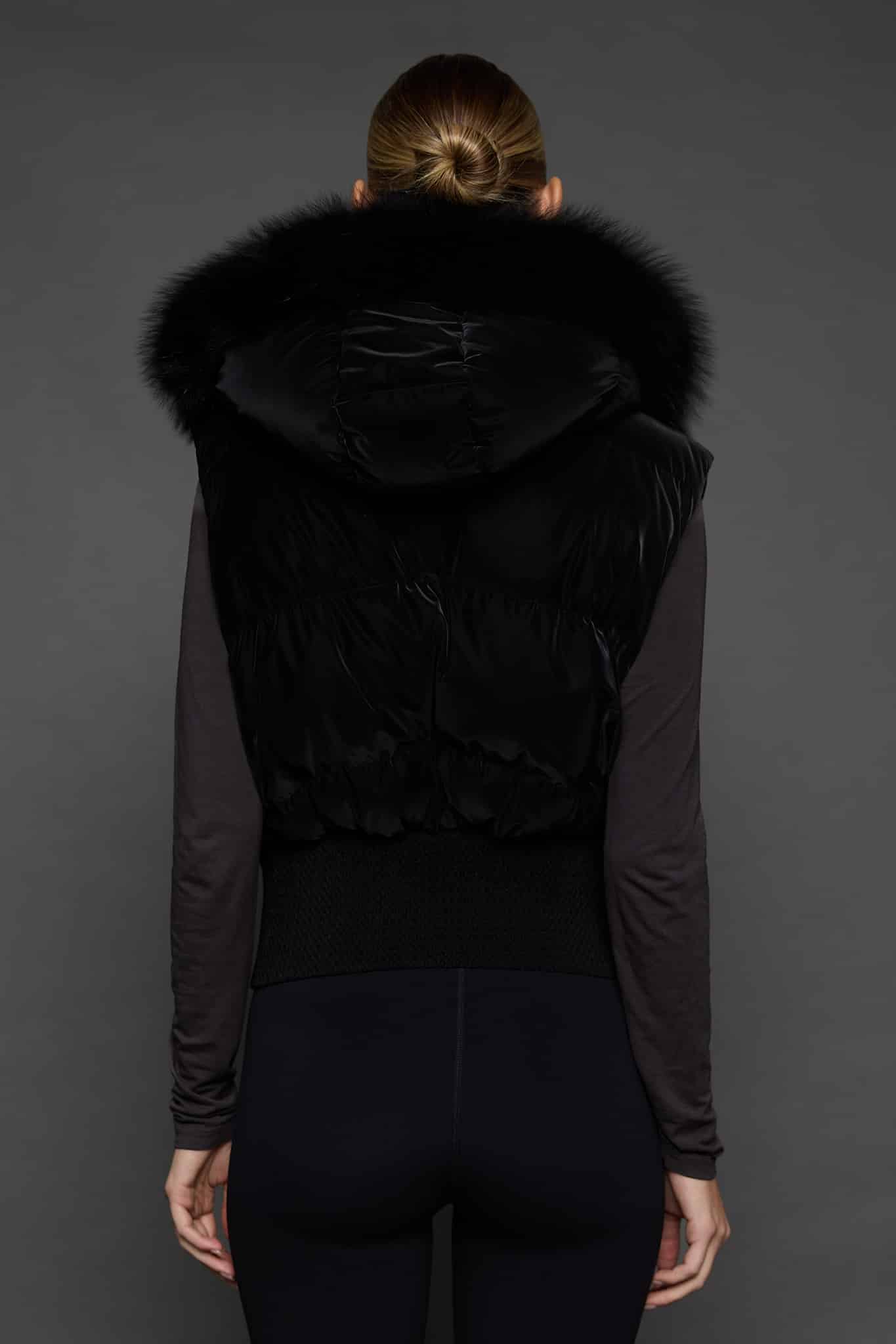 the back of a woman in a black vest against a grey background