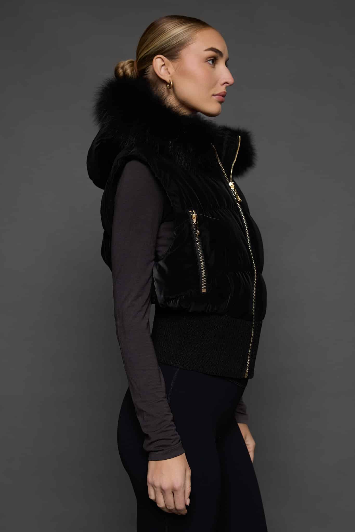 the side of a woman in a black vest against a grey background