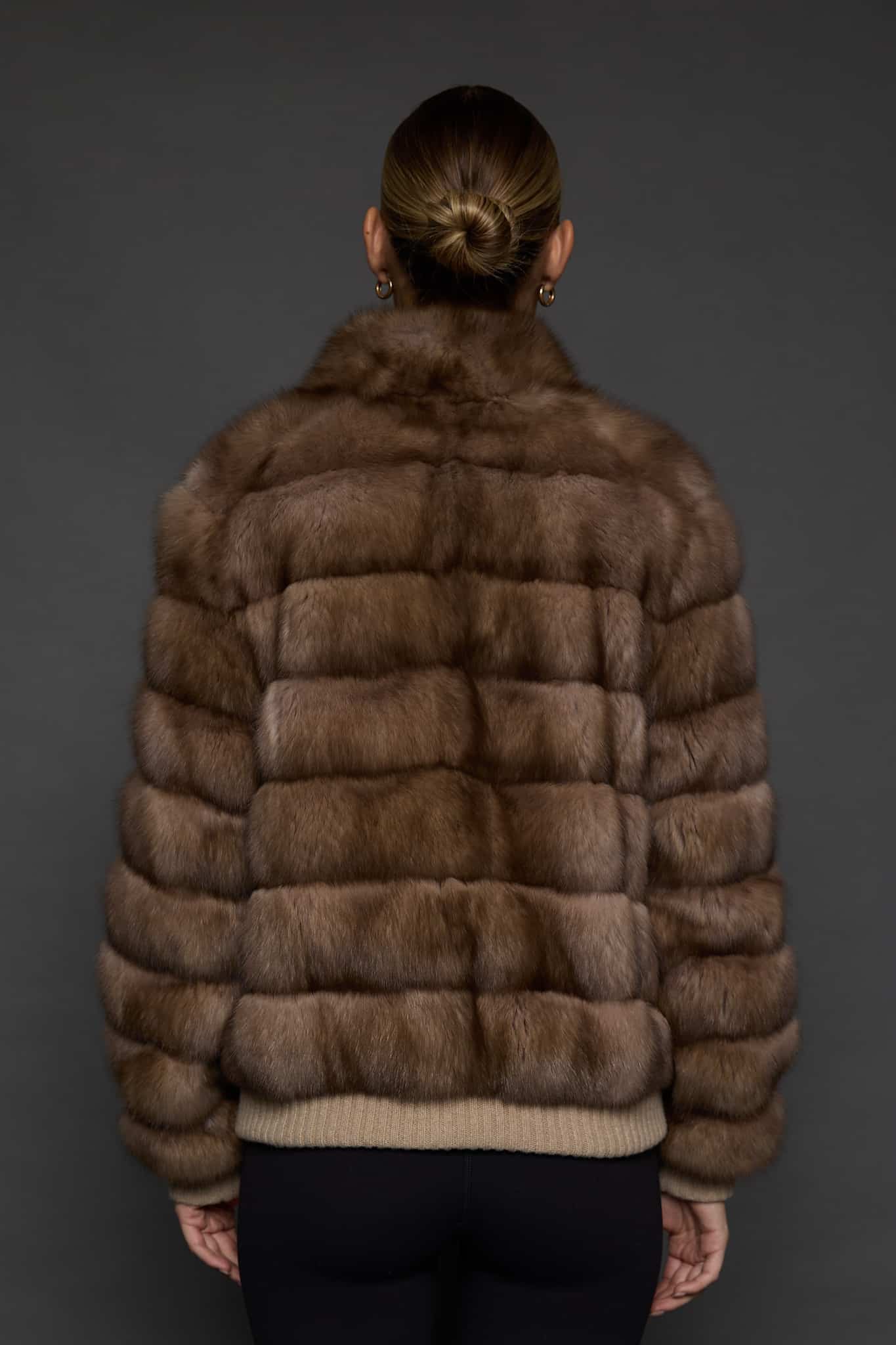 Rear view of a woman in a brown cashmere jacket with the sable side out facing a dark grey background
