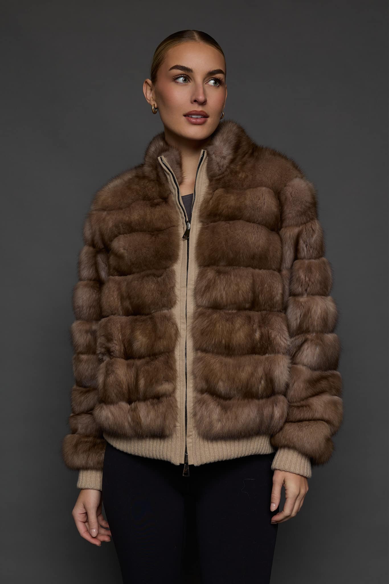 Frontal view of a woman in a brown cashmere jacket with the sable side out against a dark grey background