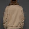 Rear view of a woman in a brown cashmere jacket with the cashmere side out facing a dark grey background