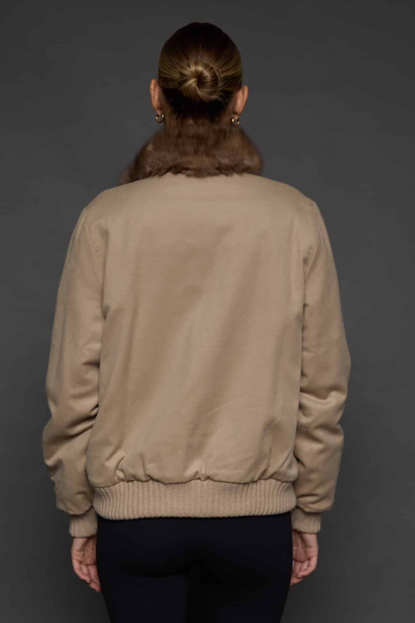 Rear view of a woman in a brown cashmere jacket with the cashmere side out facing a dark grey background