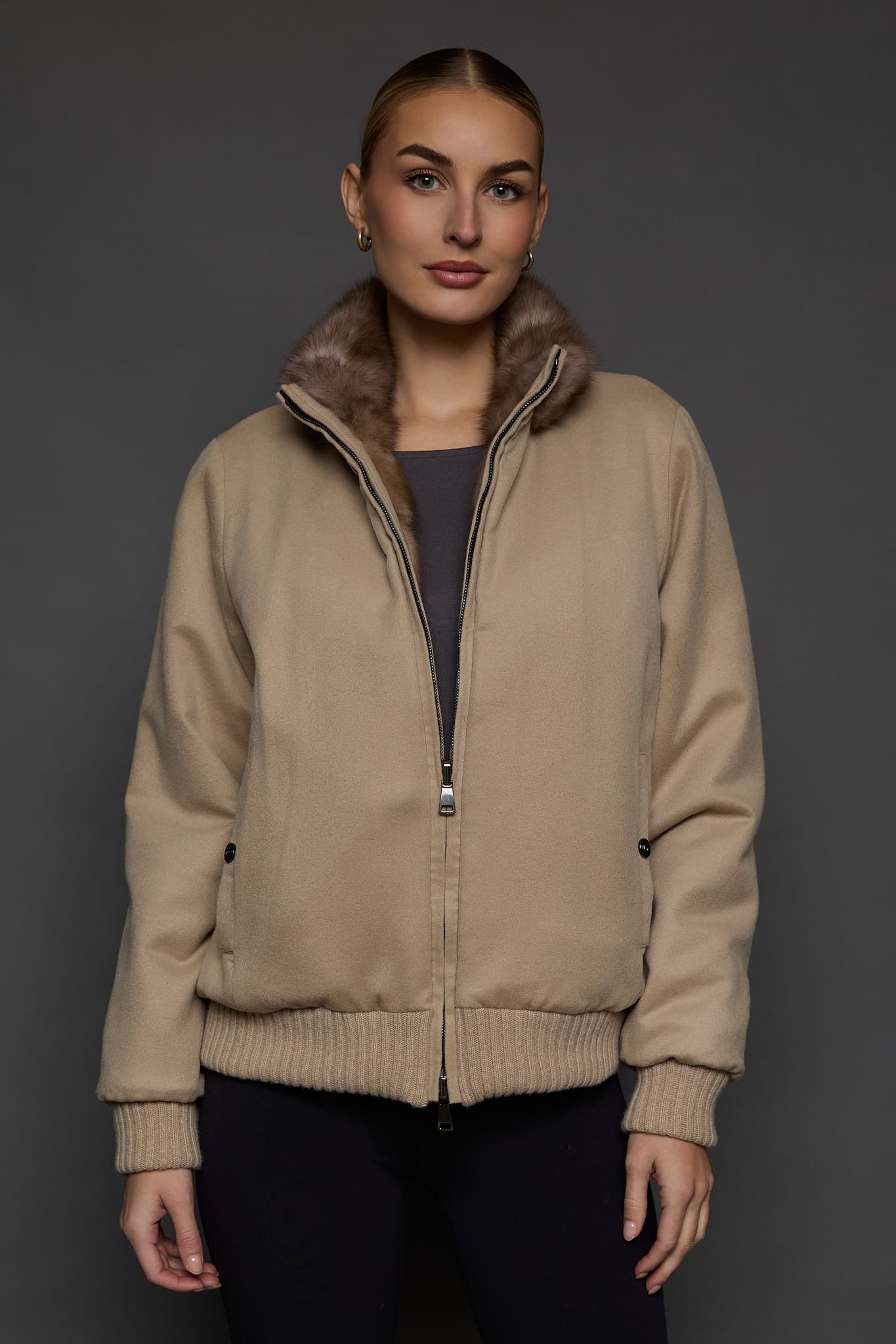 Frontal view of a woman in a brown cashmere jacket with the cashmere side out against a dark grey background