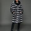 ECOMMWOMENS20255566 Frontal view of a woman in a natural empress chinchilla coat with her hands in the pockets standing in front of a grey background.