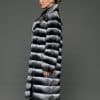 ECOMMWOMENS20255569 Profile shot of a woman in a natural empress chinchilla coat with her hands at her side standing in front of a grey background.