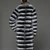 ECOMMWOMENS20255576 Rear view of a woman in a natural empress chinchilla coat standing in front of a grey background.