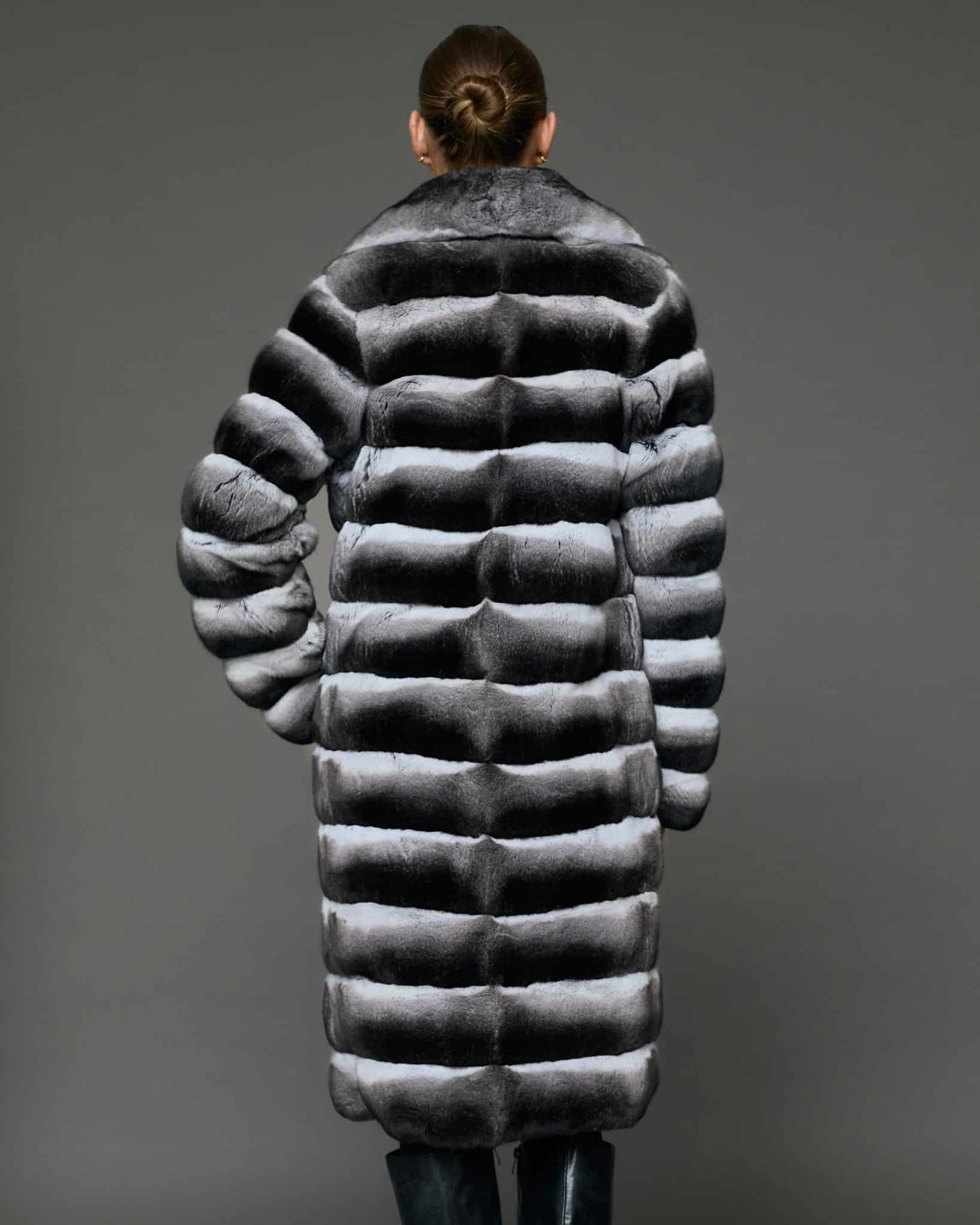 ECOMMWOMENS20255576 Rear view of a woman in a natural empress chinchilla coat standing in front of a grey background.