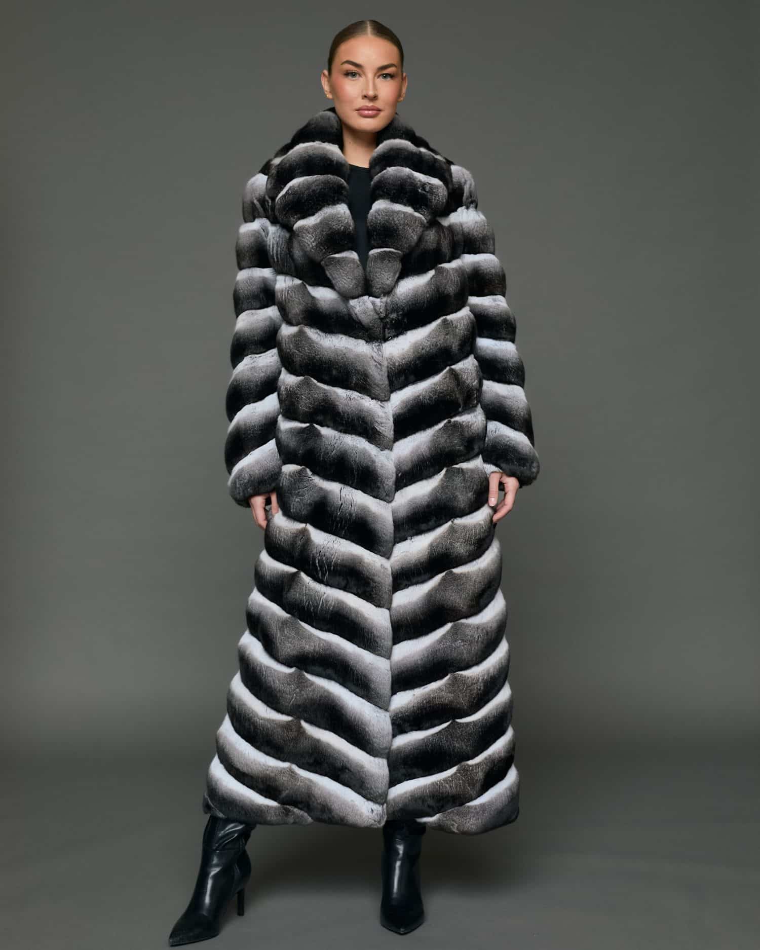 Frontal view of a woman in a natural chinchilla full length coat that is closed, standing against a grey background