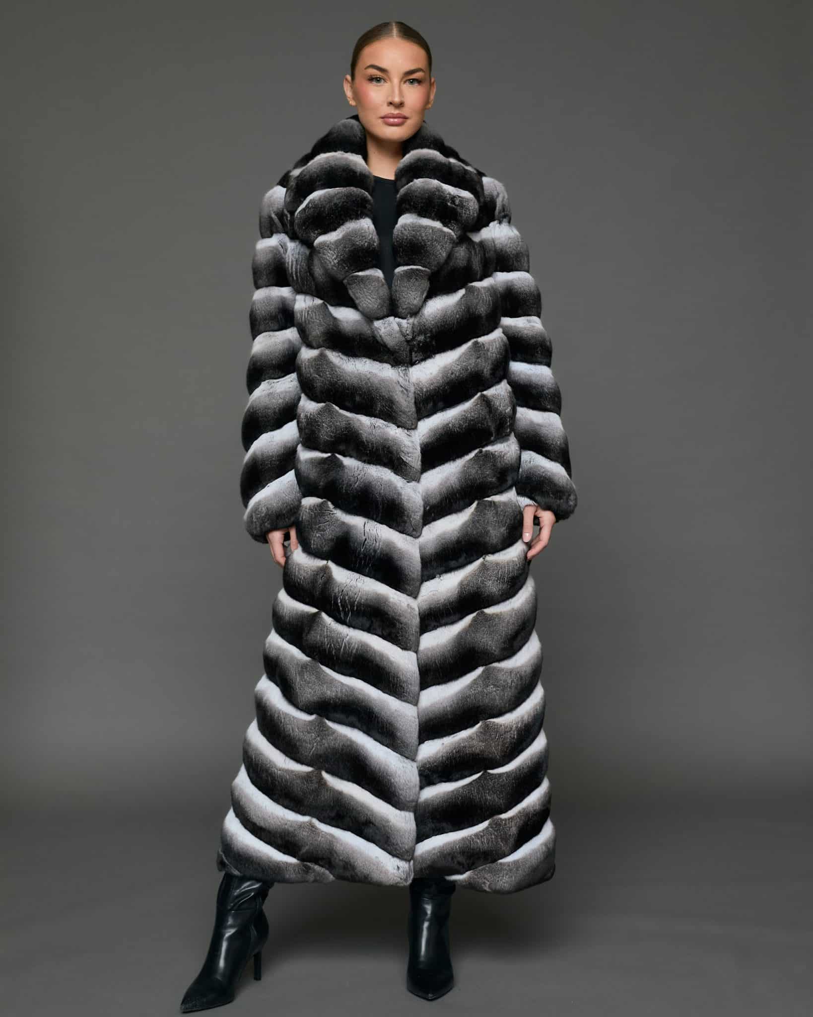 ECOMMWOMENS20255580 Frontal view of a woman in a natural chinchilla full length coat that is closed, standing against a grey background