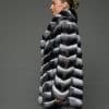 Profile view of a woman in a stroller length chinchilla coat with a shawl collar standing in front of a grey background