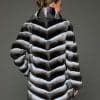 Rear view of a woman in a stroller length chinchilla coat with a shawl collar facing a grey background