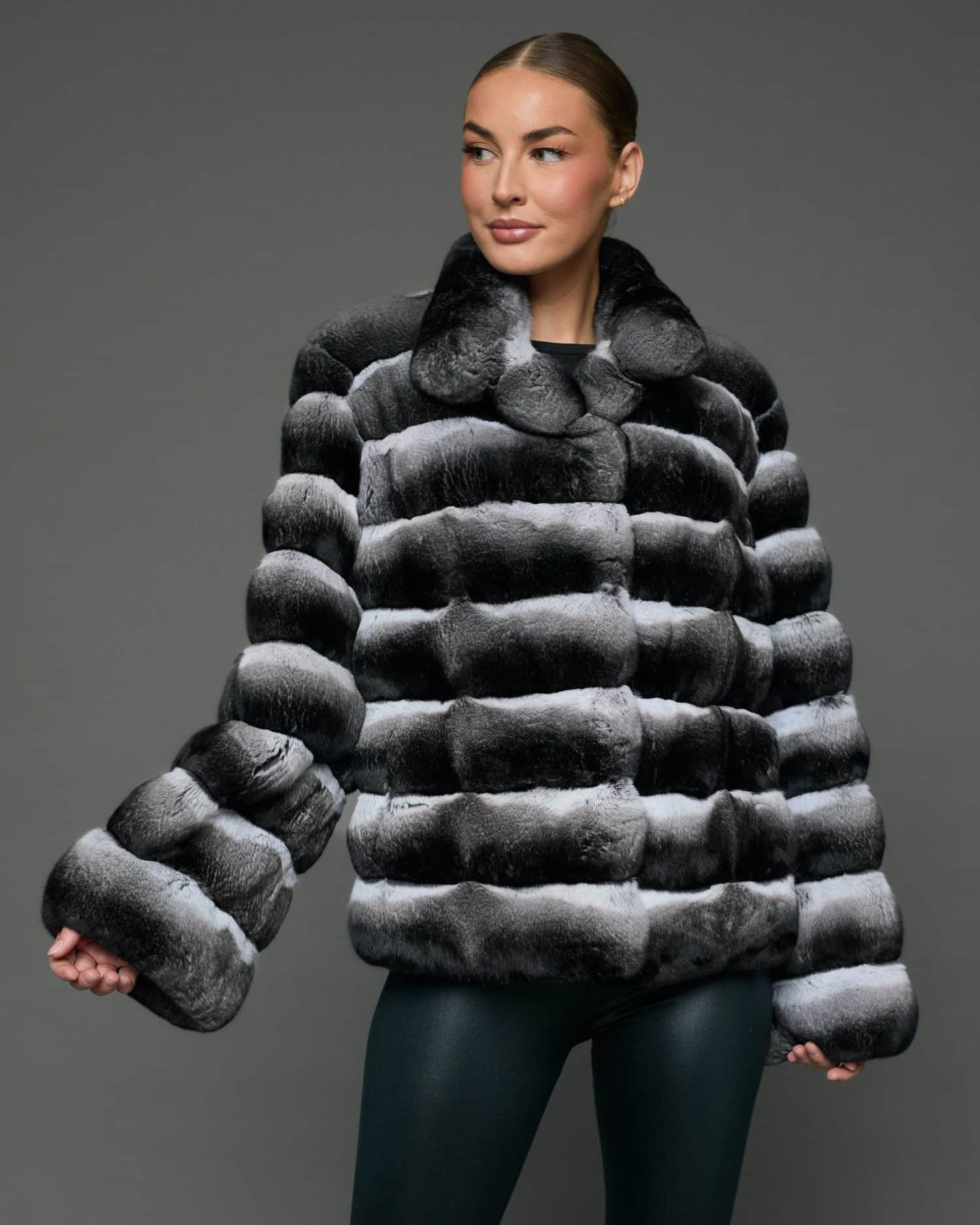 Frontal view of a woman in a natural chinchilla jacket with wing collar standing in front of a grey background