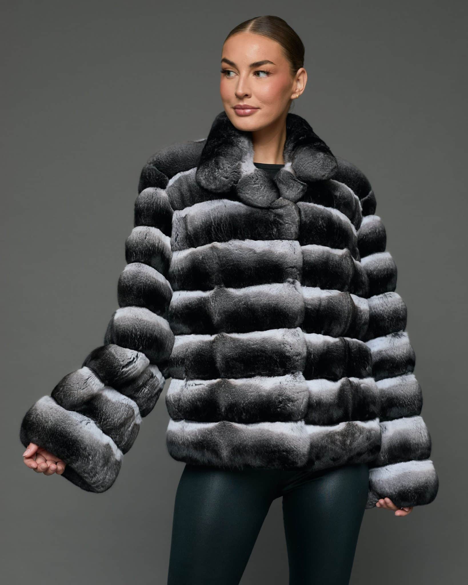 ECOMMWOMENS20255638 Frontal view of a woman in a natural chinchilla jacket with wing collar standing in front of a grey background