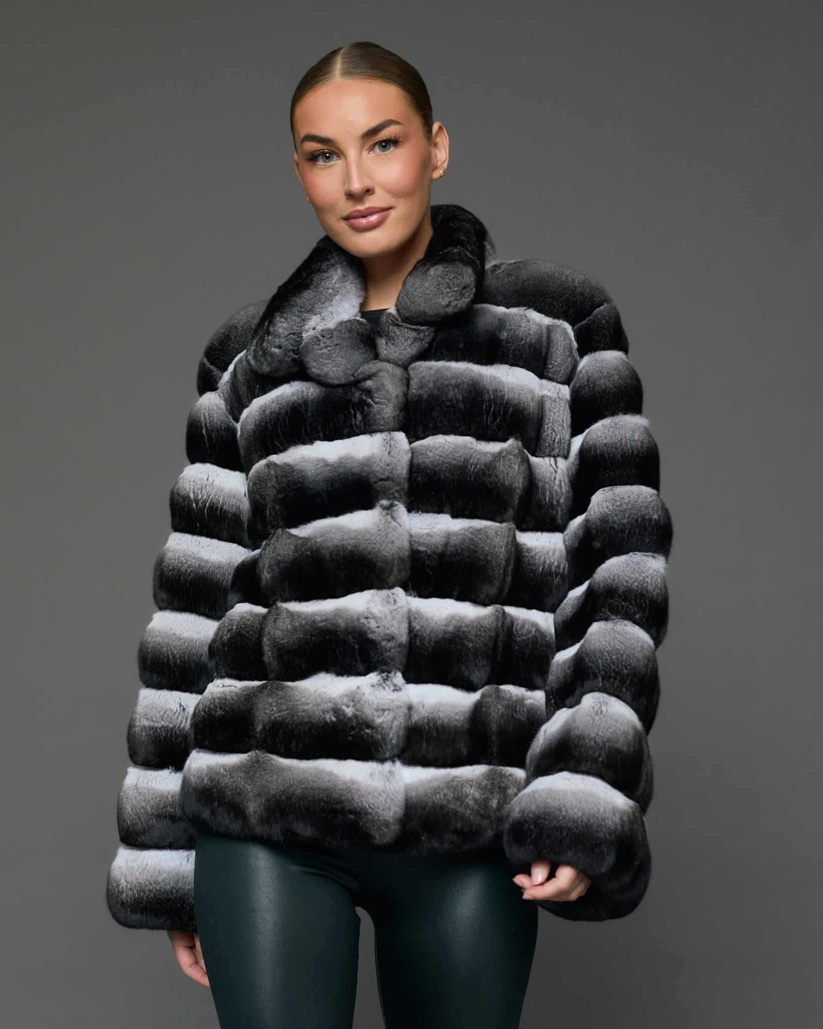ECOMMWOMENS20255640 Frontal view of a woman in a natural black and white chinchilla jacket with her arms at her sides standing in front of a grey background