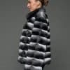 ECOMMWOMENS20255645 Profile view of a woman in a natural black and white chinchilla jacket with her arms at her sides standing in front of a grey background