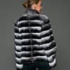 ECOMMWOMENS20255651 Rear view of a woman in a natural black and white chinchilla jacket with her arms at her sides facing a grey background