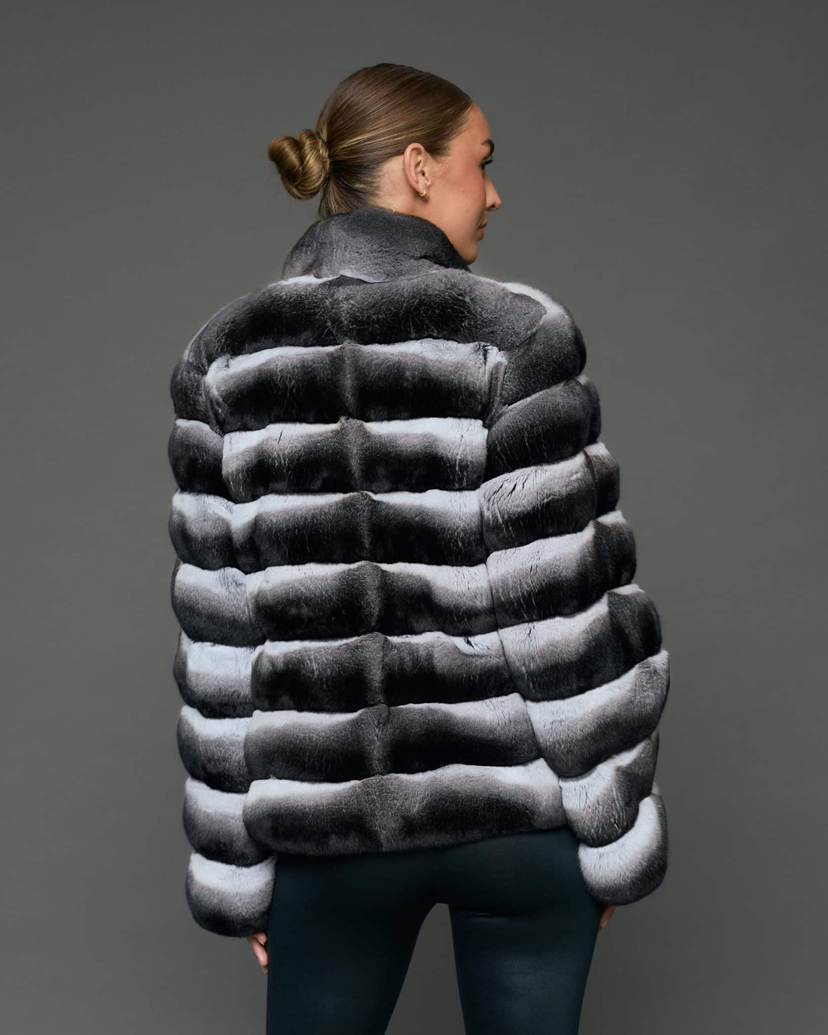 ECOMMWOMENS20255651 Rear view of a woman in a natural black and white chinchilla jacket with her arms at her sides facing a grey background