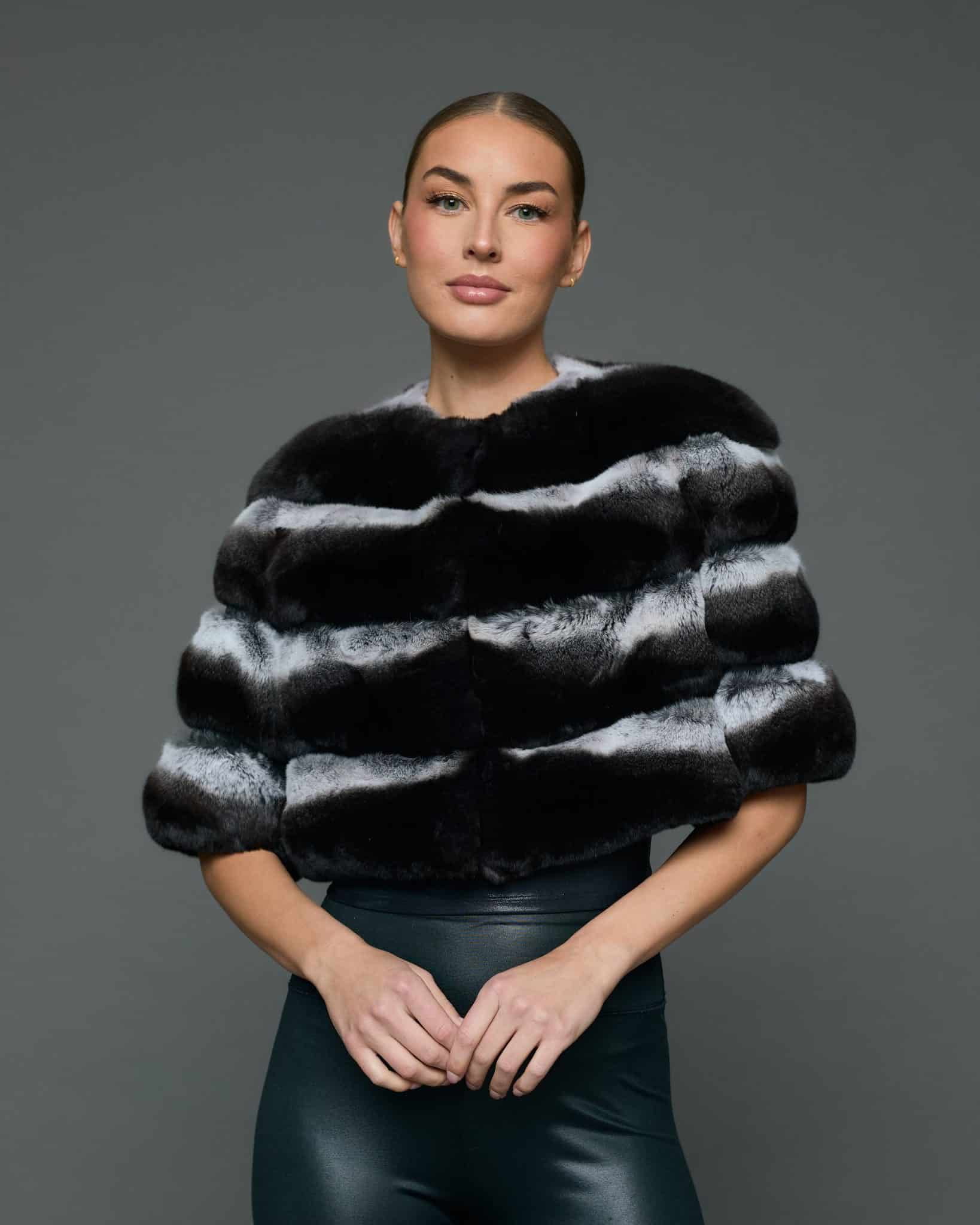 Frontal view of a woman in a natural chinchilla stole / cape with her hands together standing in front of a grey background