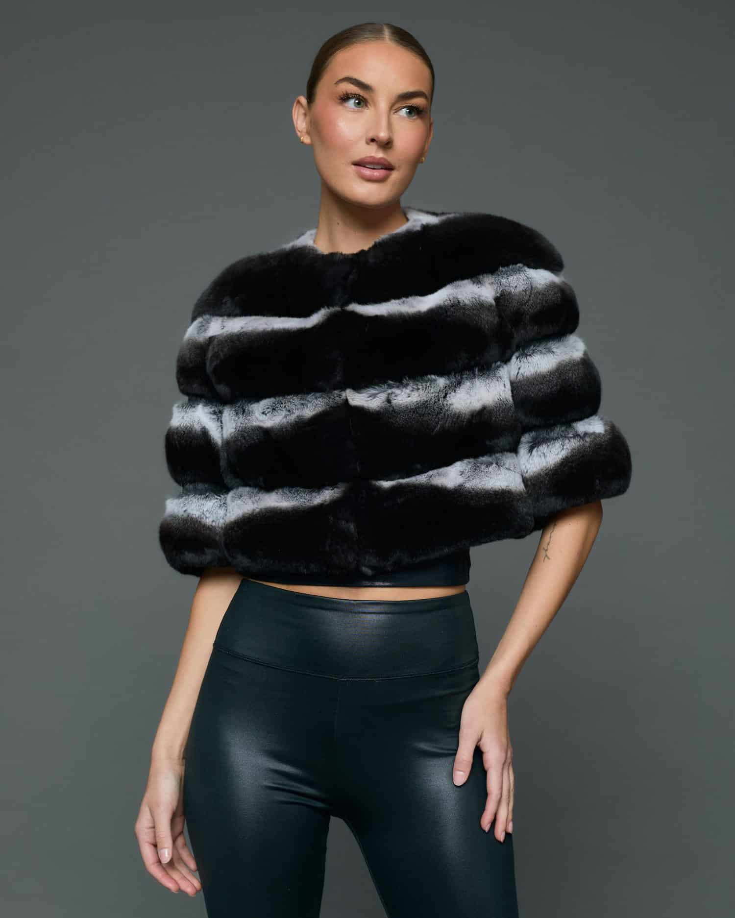 Frontal view of a woman in a natural chinchilla stole / cape with her left hand on her hip standing in front of a grey background