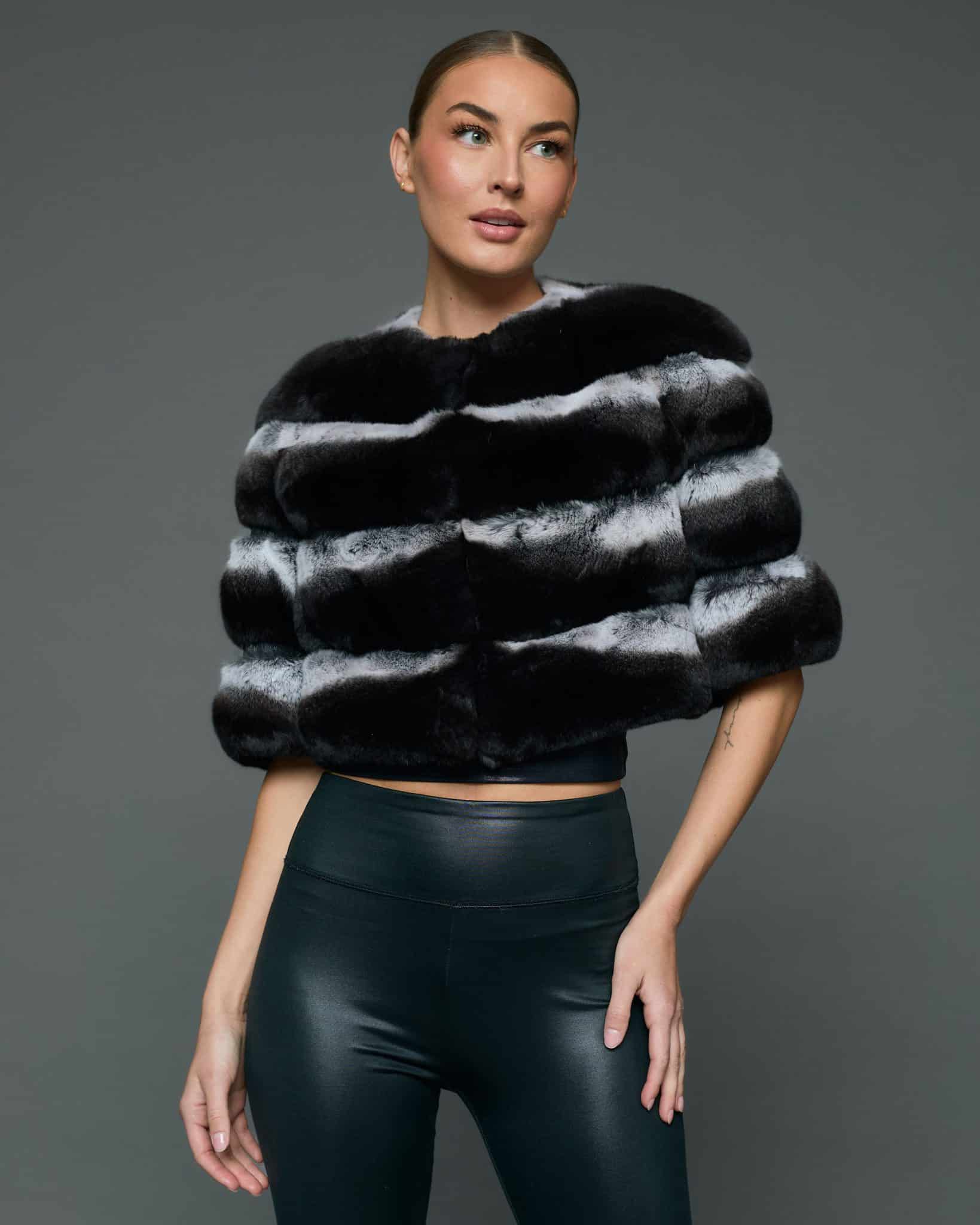 Frontal view of a woman in a natural chinchilla stole / cape with her left hand on her hip standing in front of a grey background