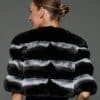 Rear shot of a woman in a natural chinchilla stole / cape standing in front of a grey background
