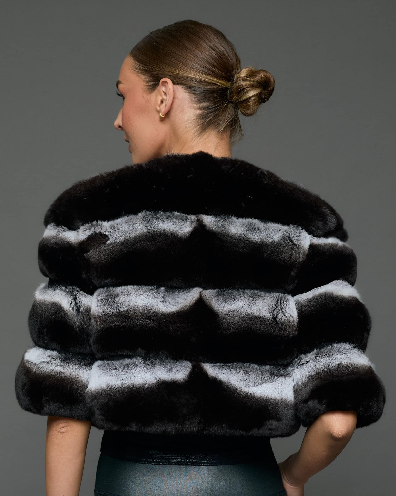 Rear shot of a woman in a natural chinchilla stole / cape standing in front of a grey background