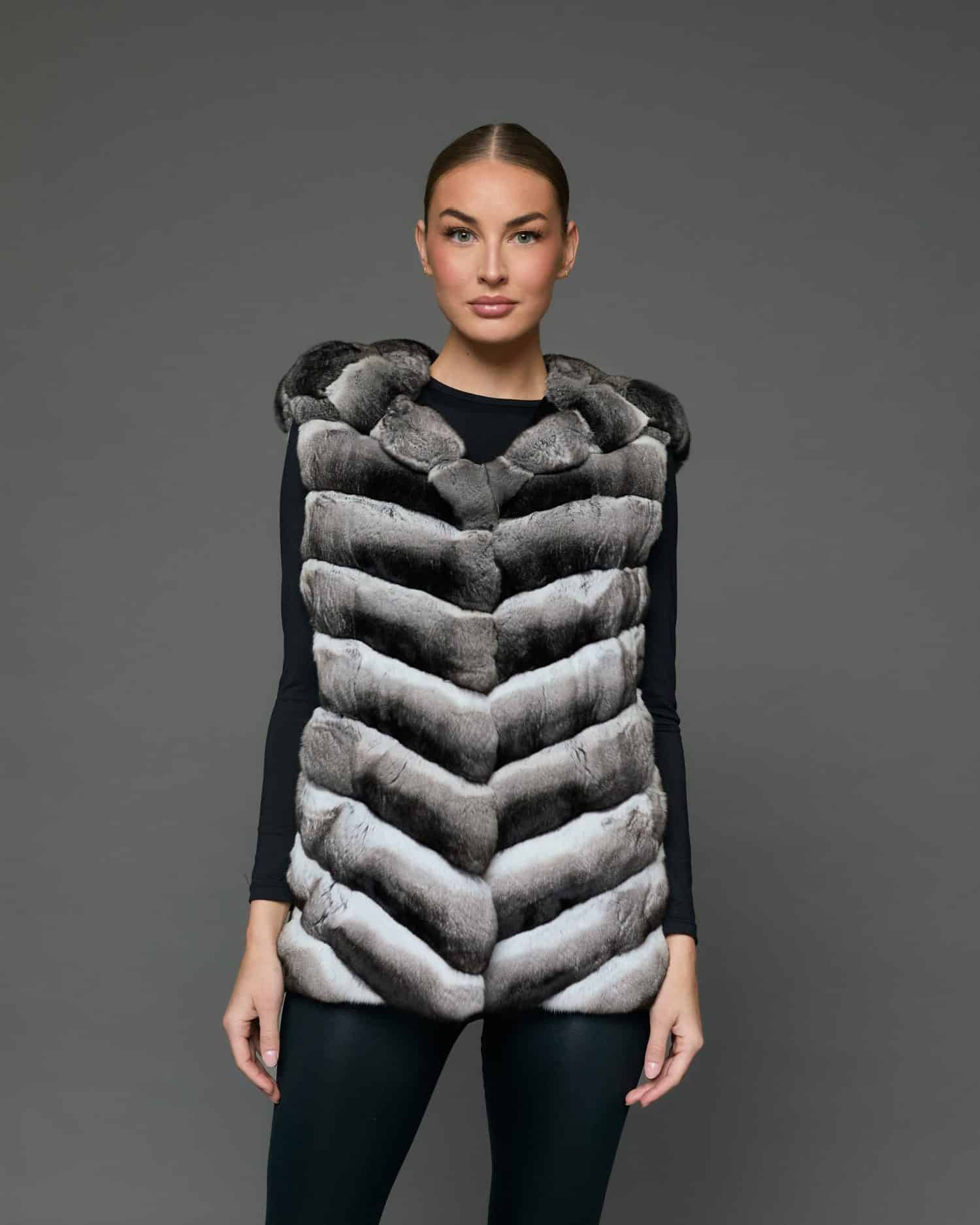 Frontal view of a woman in a sleeveless chinchilla vest standing against a grey background