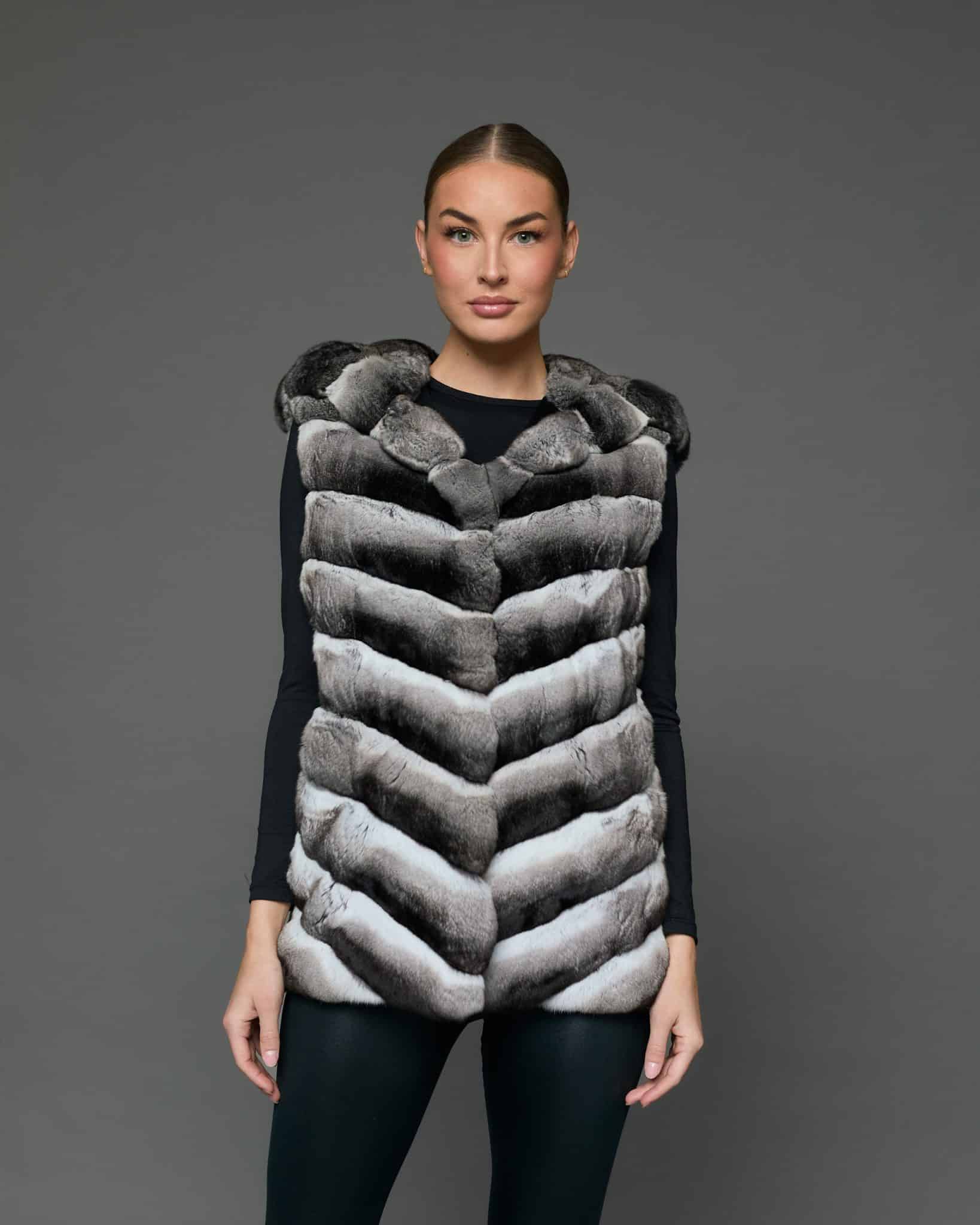Frontal view of a woman in a sleeveless chinchilla vest standing against a grey background