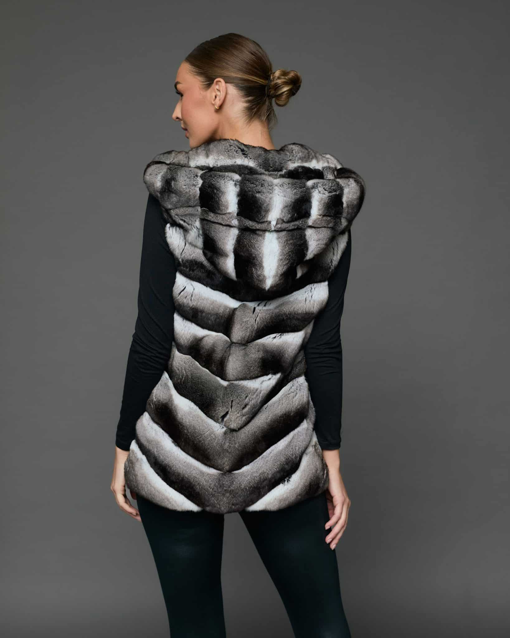 Rear view of a woman in a sleeveless chinchilla vest standing against a grey background