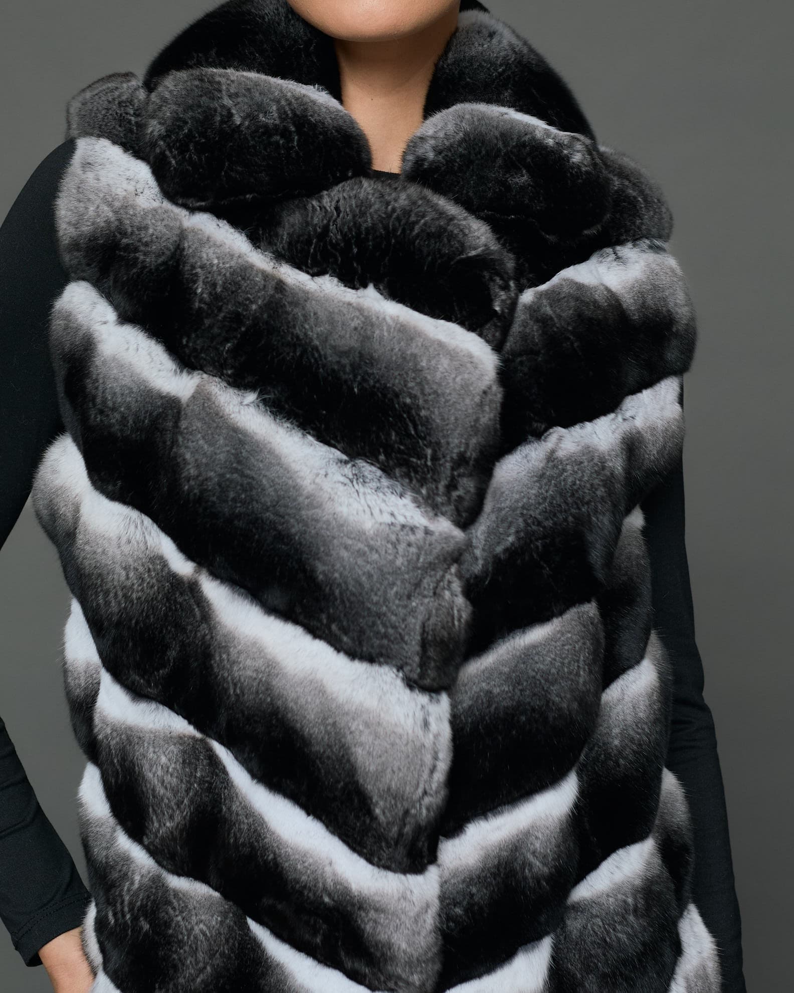 Close-up view of a knee-length black and white chinchilla vest in front of a grey background