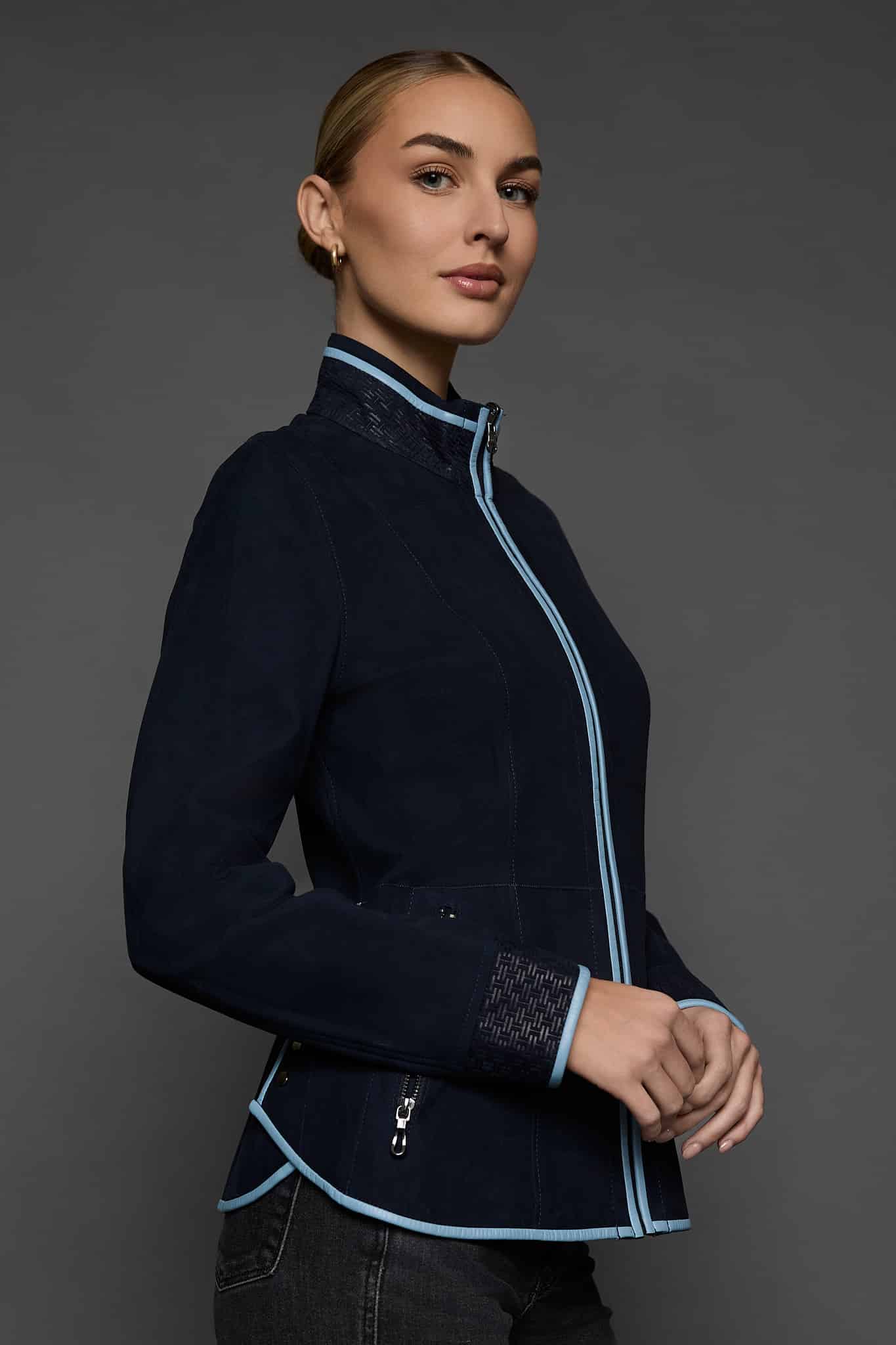 IMANI NAVY BLUE JACKET SIDE the side of a woman in a dark blue jacket against a grey background