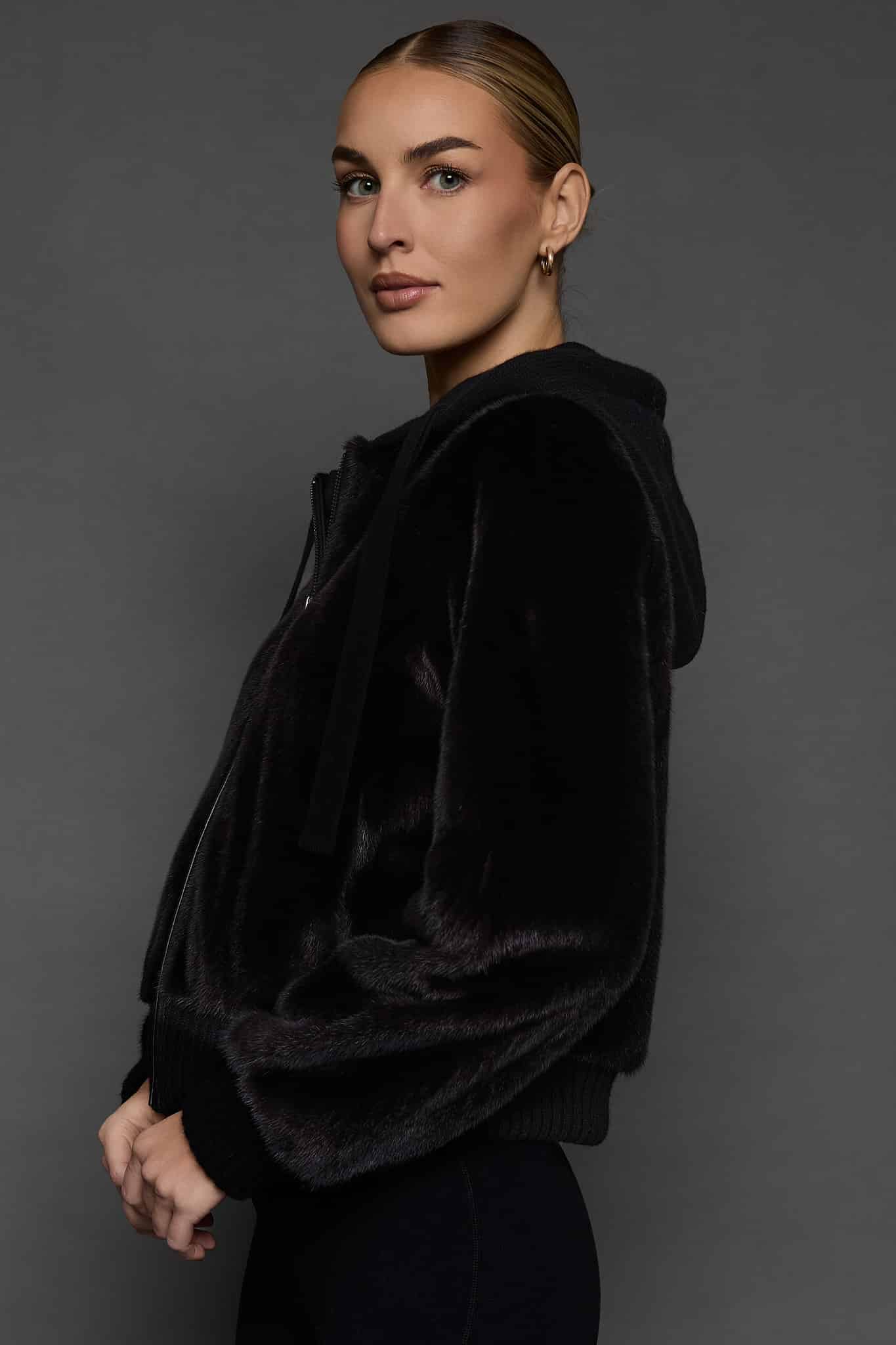 the side of a woman in a black jacket against a white background