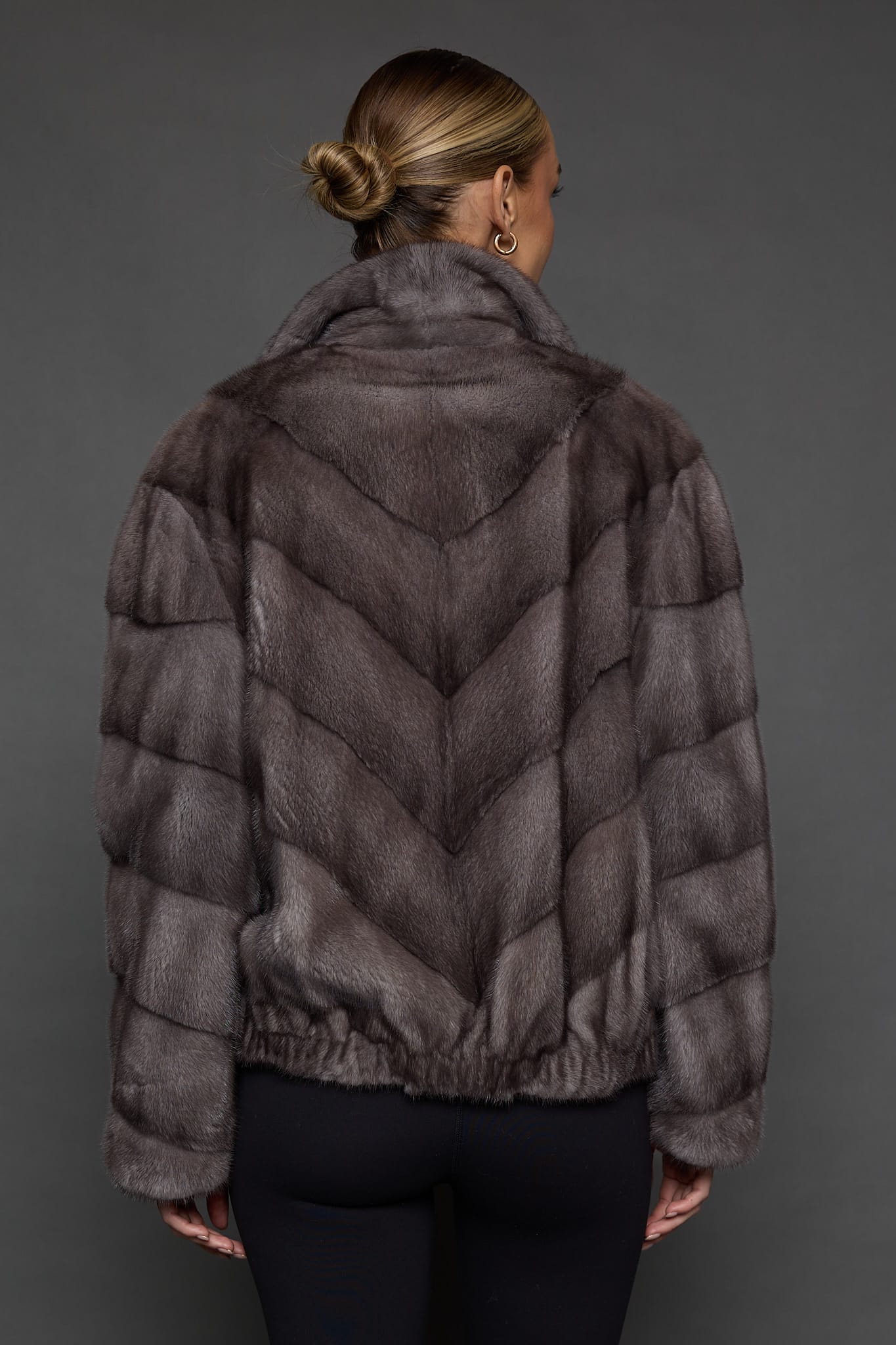 Rear view of a woman in a pastel blue mink jacket standing in front of a dark grey background.