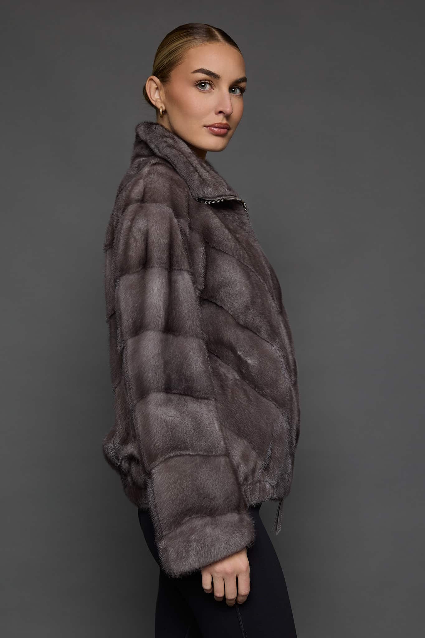 Profile view of a woman in a blue pastel colored mink jacket standing in front of a dark grey background.