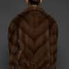 Rear view of a woman in a brown mink jacket facing a dark grey background.