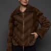 Frontal view of a woman in a brown mink jacket standing in front of a dark grey background.