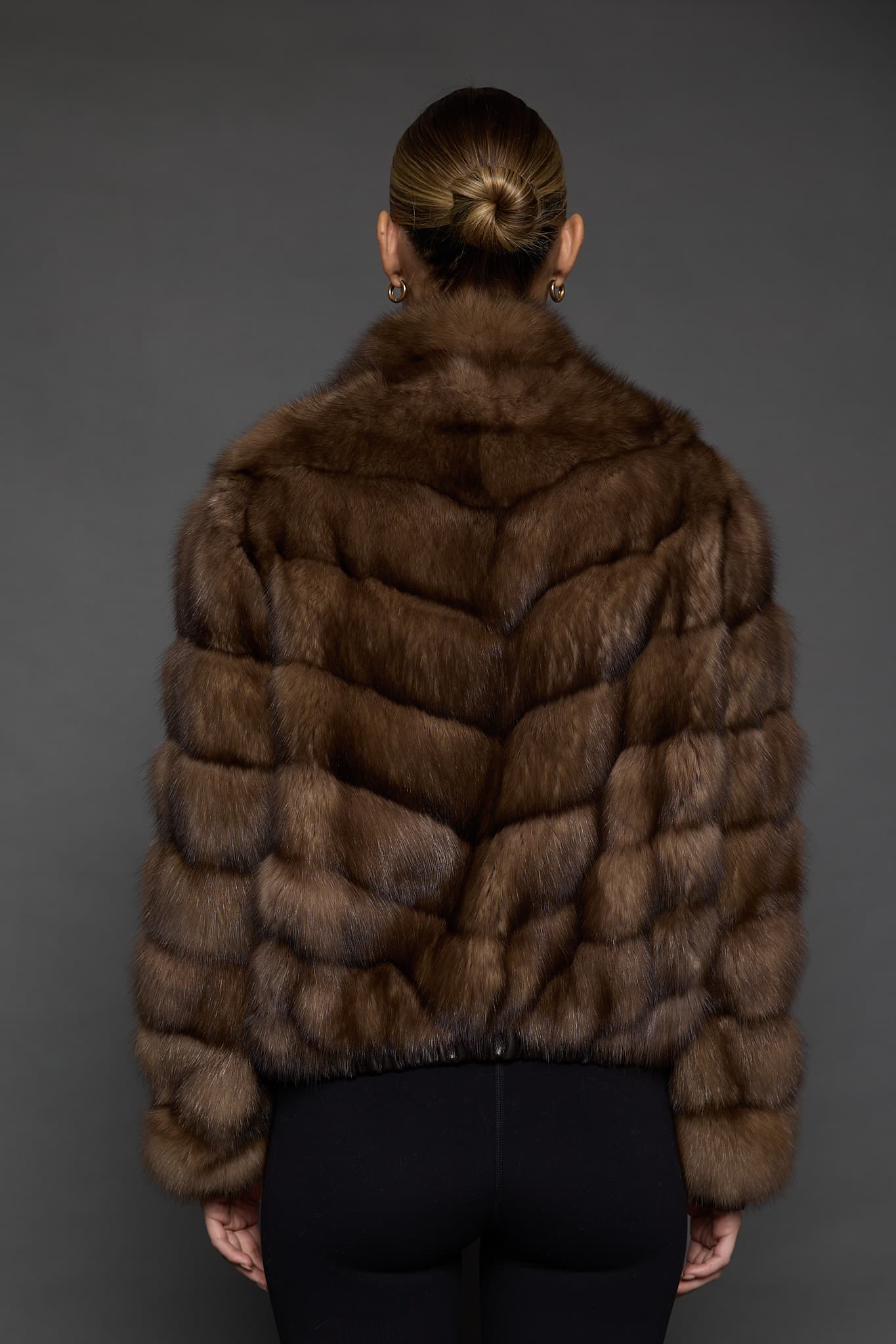 Rear view of a woman in a Russian sable jacket standing in front of a dark grey background