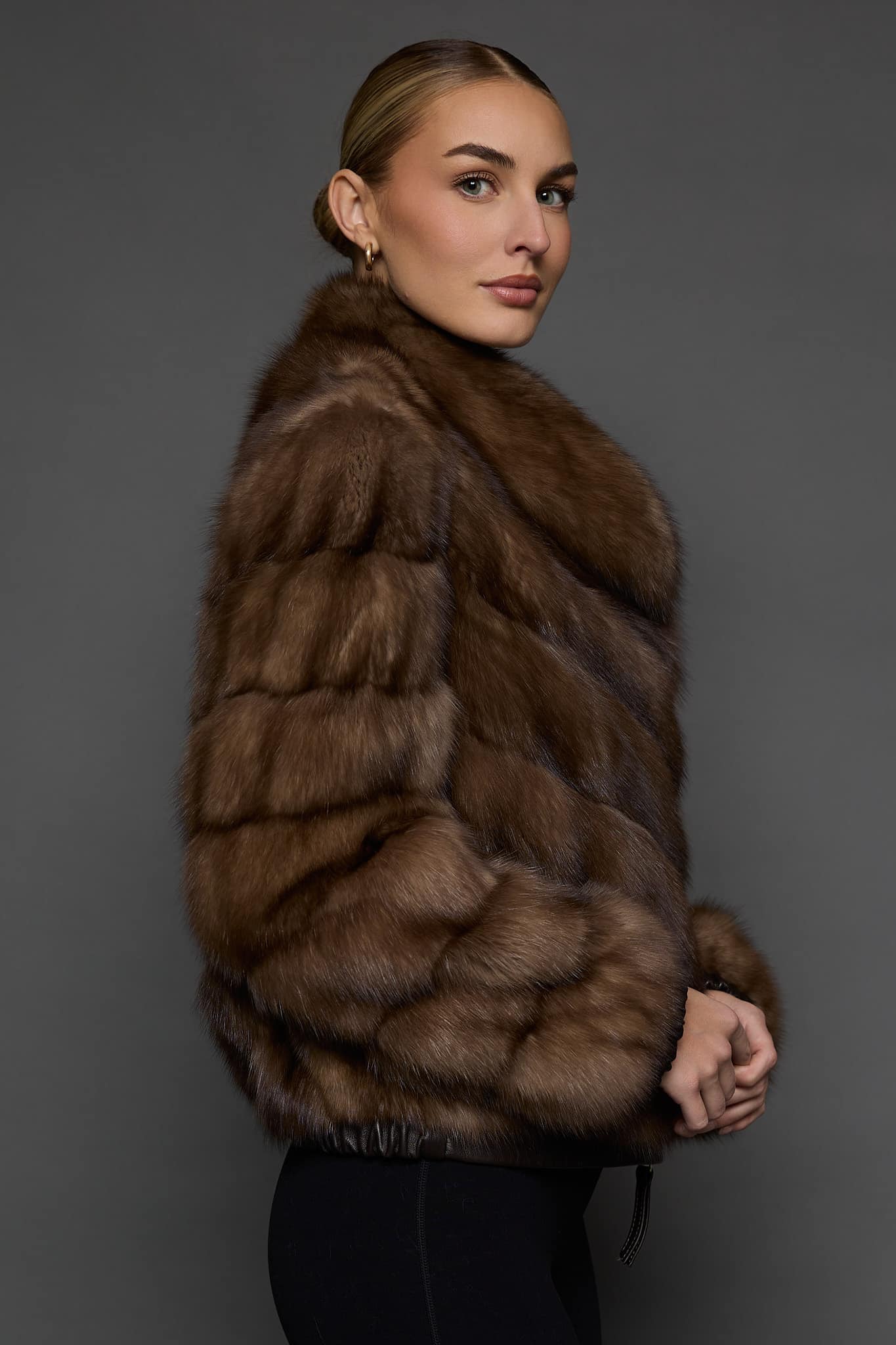 Side view of a woman in a Russian sable jacket standing in front of a dark grey background