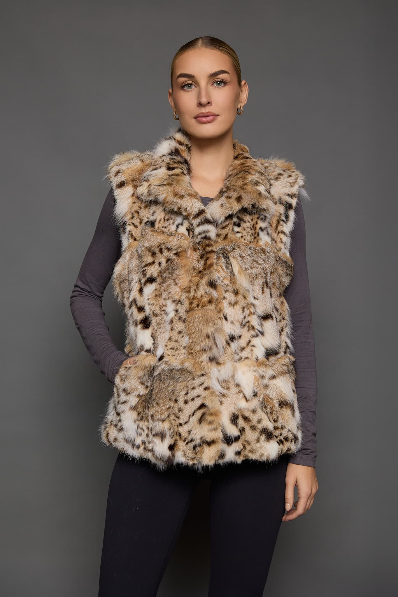 Frontal view of a woman in a sculpted American lynx vest with her right hand in the front pocket, standing in front of a grey background
