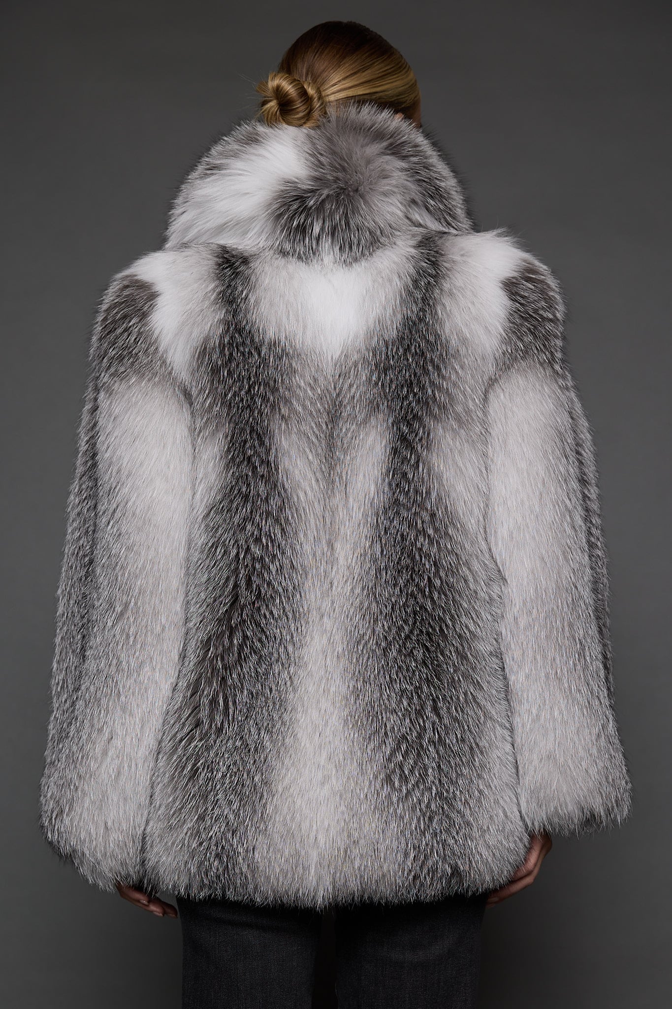 the back of a woman in a white grey fur coat against a grey background