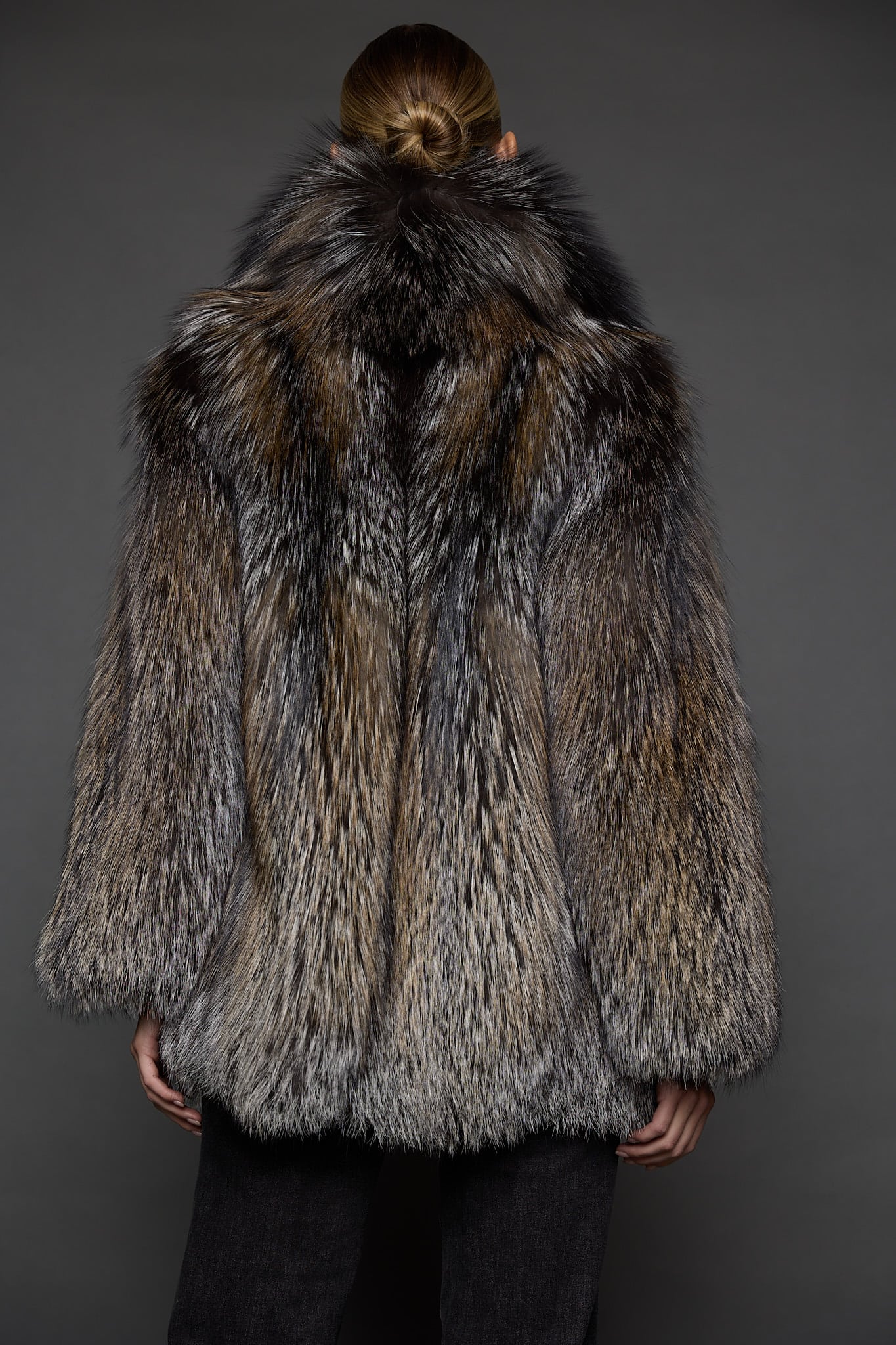 the back of a woman in a brown fur coat against a grey background