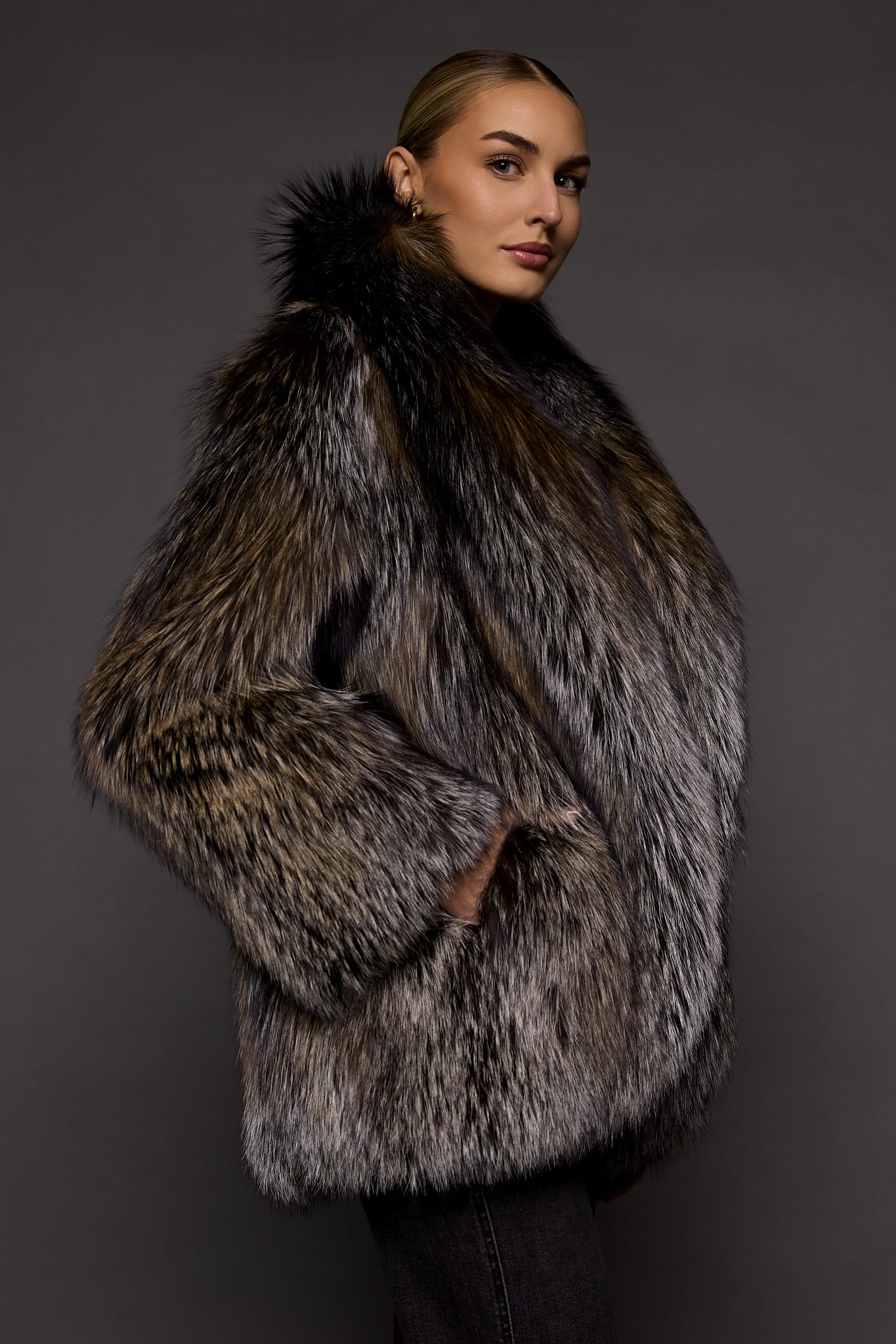 the side of a woman in a brown fur coat against a grey background