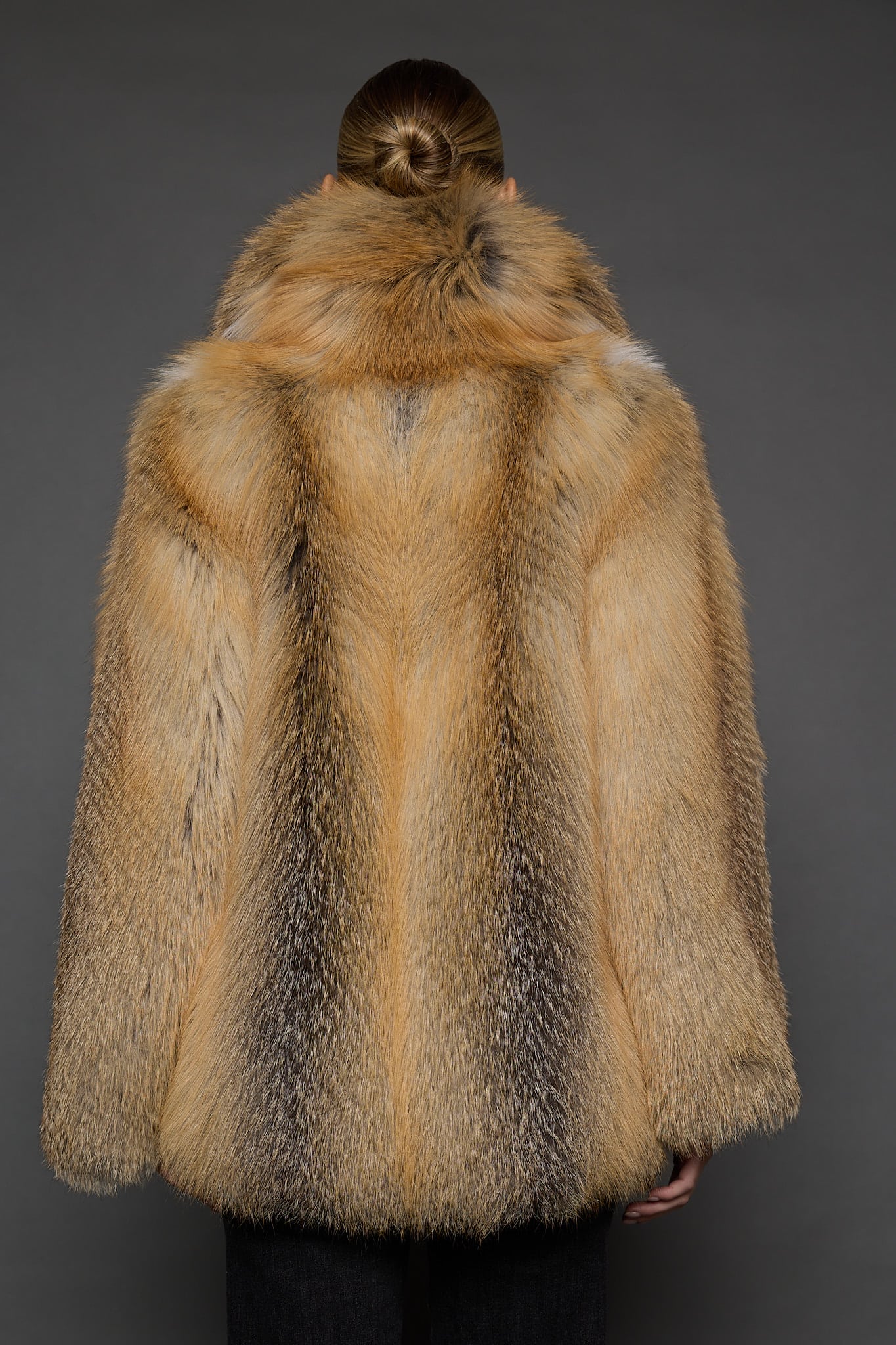 the back of a a woman in a red fur coat against a grey background
