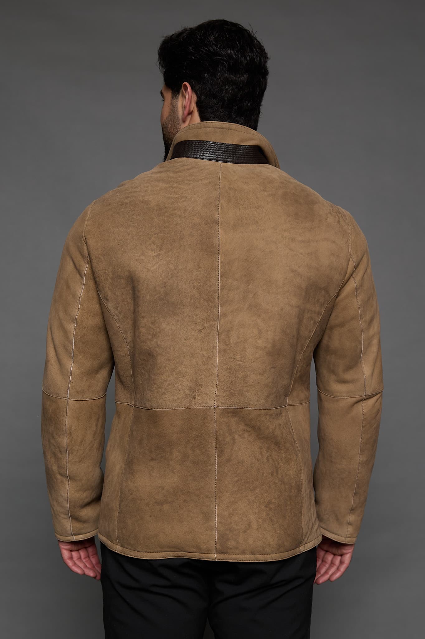the back of a man in a tan coat against a grey background
